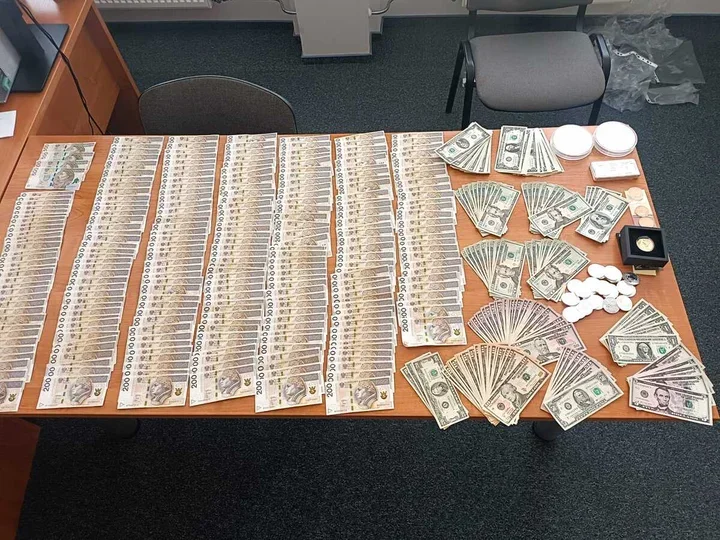 Na biurku w pomieszczeniu biurowym ułożono duże ilości banknotów polskich i amerykańskich oraz monety i drobne przedmioty.
