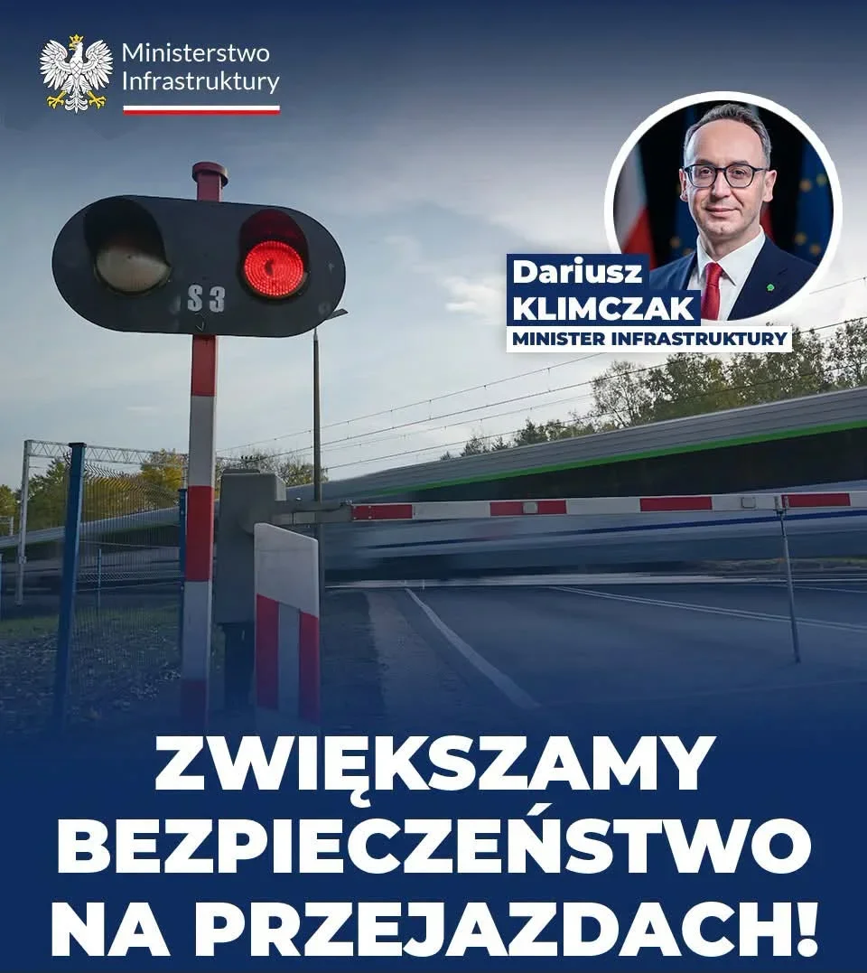 Plakat Ministerstwa Infrastruktury z sygnalizatorem świetlnym na przejeździe kolejowym i hasłem o zwiększaniu bezpieczeństwa.