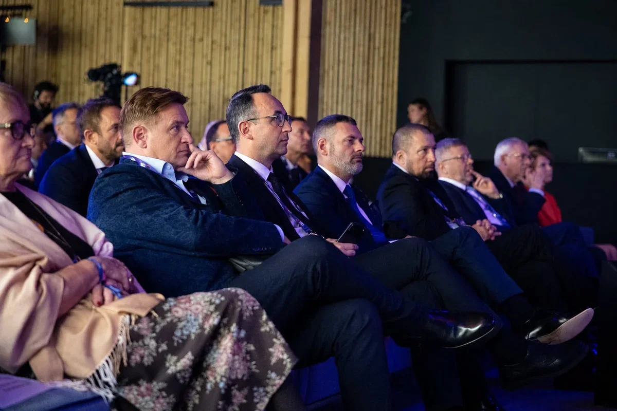 Uczestnicy konferencji lub wydarzenia formalnego siedzą w rzędach i słuchają prelegenta.