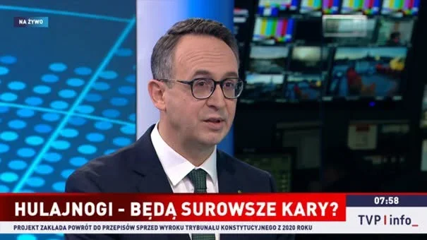 Mężczyzna w garniturze i okularach udziela wywiadu w studiu telewizyjnym TVP Info podczas porannej audycji na żywo.