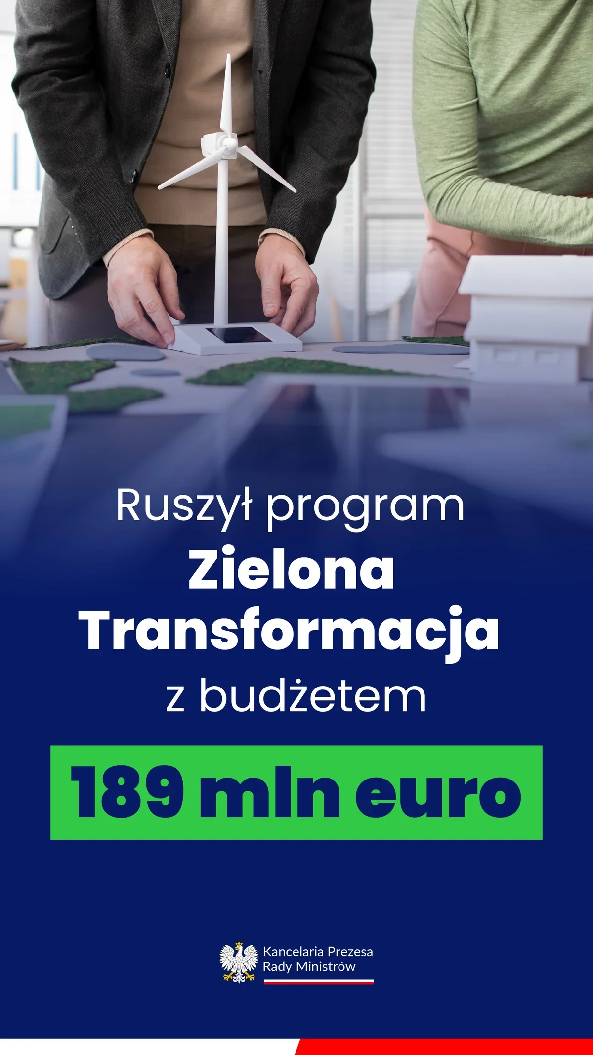 Dwie osoby stoją przy stole z makietą przedstawiającą model wiatraka, budynek i zieleń, na dole grafika informacyjna o programie Zielona Transformacja.
