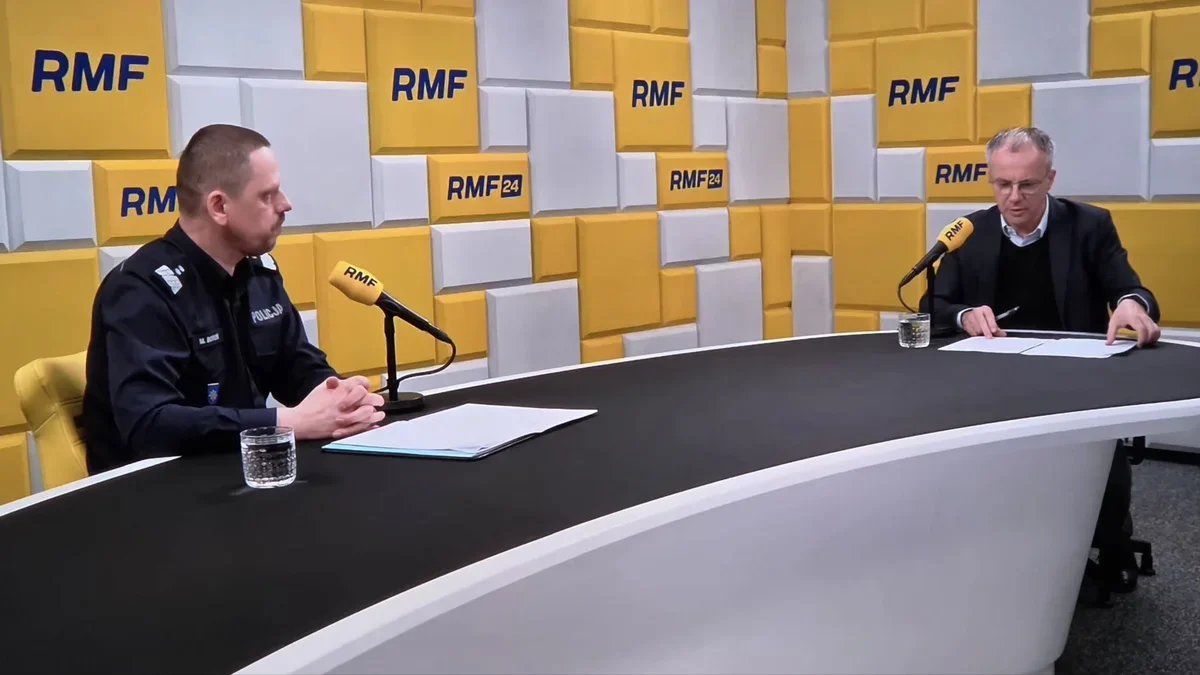Policjant i mężczyzna w garniturze siedzą przy stole w studiu radiowym RMF podczas wywiadu.