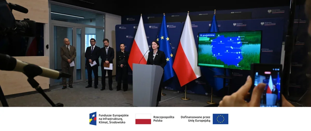 Kobieta wygłasza przemówienie przy mównicy w towarzystwie mężczyzn i kobiety w mundurze na tle flag Polski i Unii Europejskiej.