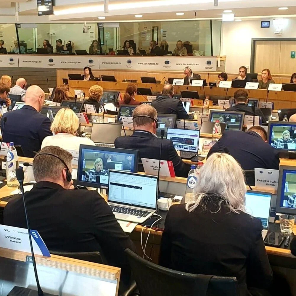 Uczestnicy konferencji lub posiedzenia w sali plenarnej z tłumaczeniem symultanicznym siedzą przy biurkach z laptopami i monitorami.
