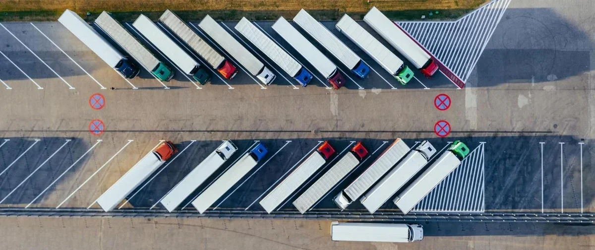 Z lotu ptaka widoczne są zaparkowane ciężarówki na dużym parkingu dla tirów wzdłuż drogi.