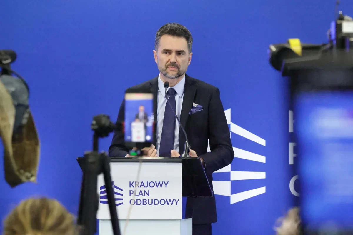 Mężczyzna w garniturze przemawia z mównicy z napisem „Krajowy Plan Odbudowy” podczas konferencji prasowej.