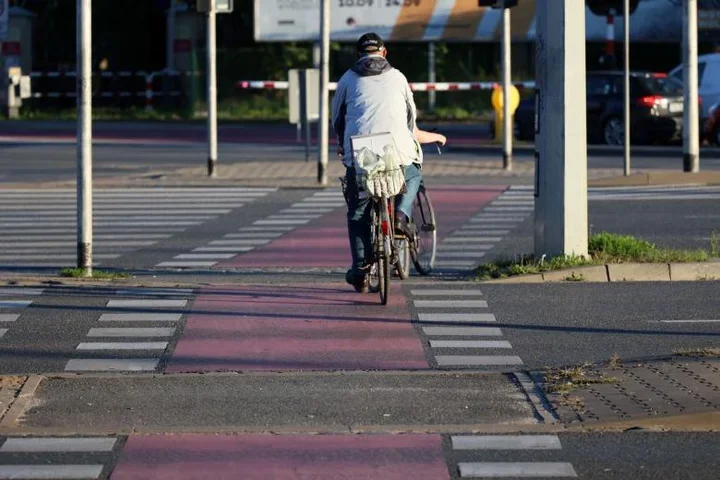 Mężczyzna jedzie na rowerze po czerwonej ścieżce rowerowej przez przejście dla pieszych na skrzyżowaniu w mieście.