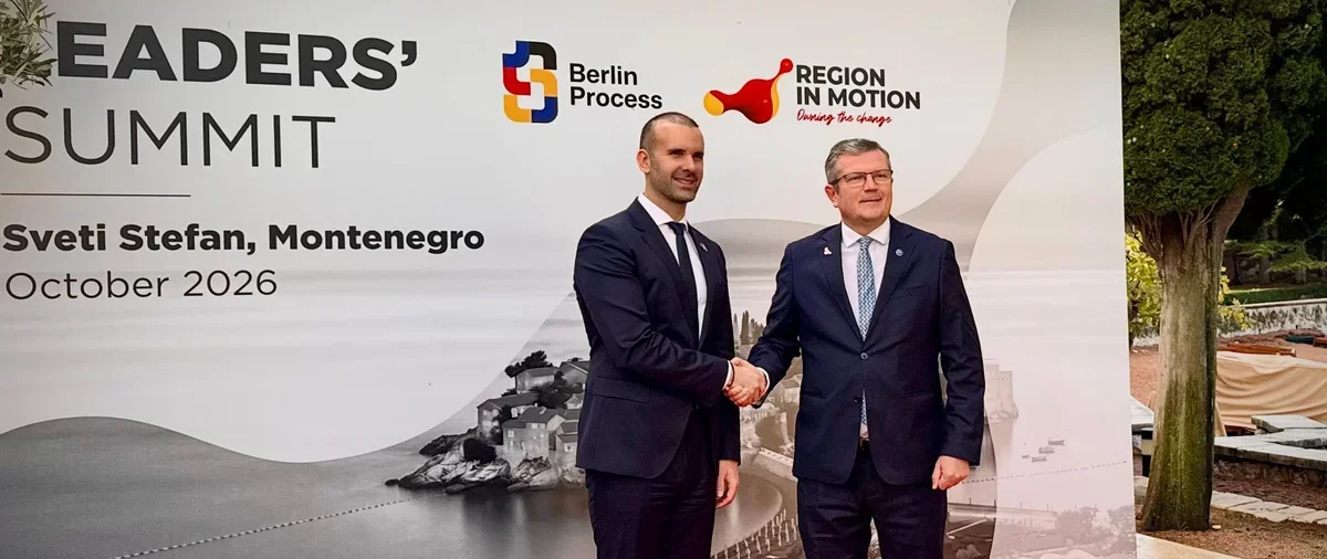 Dwaj mężczyźni w garniturach witają się uściskiem dłoni przed banerem zapowiadającym szczyt liderów w Czarnogórze w październiku 2026 roku.