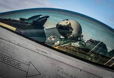 Pilot w hełmie i masce tlenowej siedzi w kokpicie myśliwca F-16C.