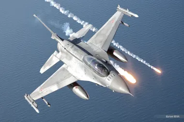 Polski myśliwiec F-16 z biało-czerwonymi znakami na skrzydłach leci nad morzem i wystrzeliwuje flary.