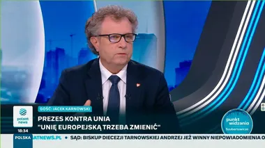 Mężczyzna w garniturze i krawacie siedzi w studiu telewizyjnym podczas programu informacyjnego, na ekranie widoczne są napisy dotyczące gościa i tematu rozmowy.