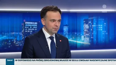 Mężczyzna w garniturze i krawacie siedzi w studiu telewizyjnym Polsat News podczas programu informacyjnego.