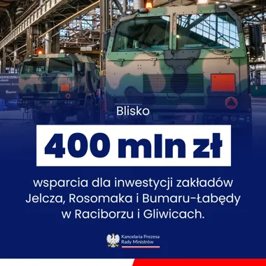 Dwa wojskowe pojazdy ciężarowe w kamuflażu stoją w hali produkcyjnej zakładu zbrojeniowego.