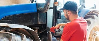 Mężczyzna w czerwonej koszulce i czapce tankuje niebieski traktor.