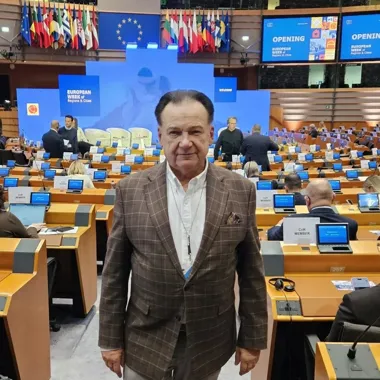 Mężczyzna w kraciastej marynarce stoi w sali plenarnej podczas otwarcia Europejskiego Tygodnia Regionów i Miast w Brukseli.