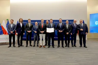 Grupa mężczyzn w garniturach pozuje do zdjęcia podczas oficjalnej uroczystości w siedzibie Ministerstwa Spraw Wewnętrznych i Administracji, jeden z nich trzyma