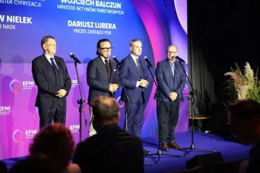 Czterech mężczyzn w garniturach stoi na scenie przed mikrofonami podczas Europejskiego Forum Nowych Idei.