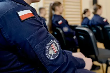 Uczniowie w mundurach z polską flagą na rękawie siedzą na krzesłach w sali, na pierwszym planie naszywka „Szkoła o Profilu Mundurowym".