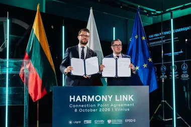 Dwaj mężczyźni w garniturach prezentują podpisane dokumenty podczas ceremonii Harmony Link w Wilnie, w tle flagi Litwy, Polski i UE.