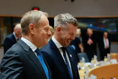 Dwaj mężczyźni w garniturach stoją w sali konferencyjnej przy okrągłym stole z butelkami i szklankami.