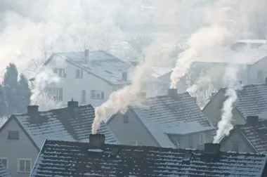 Z dymem z komina nad dachami domów w zimowej, oszronionej dzielnicy mieszkaniowej.