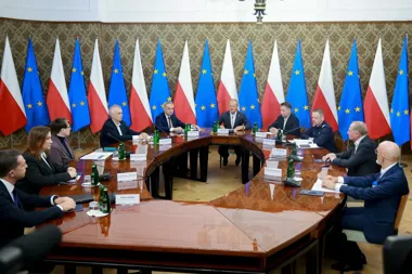 Spotkanie przy owalnym stole w reprezentacyjnej sali z flagami Polski i Unii Europejskiej w tle.