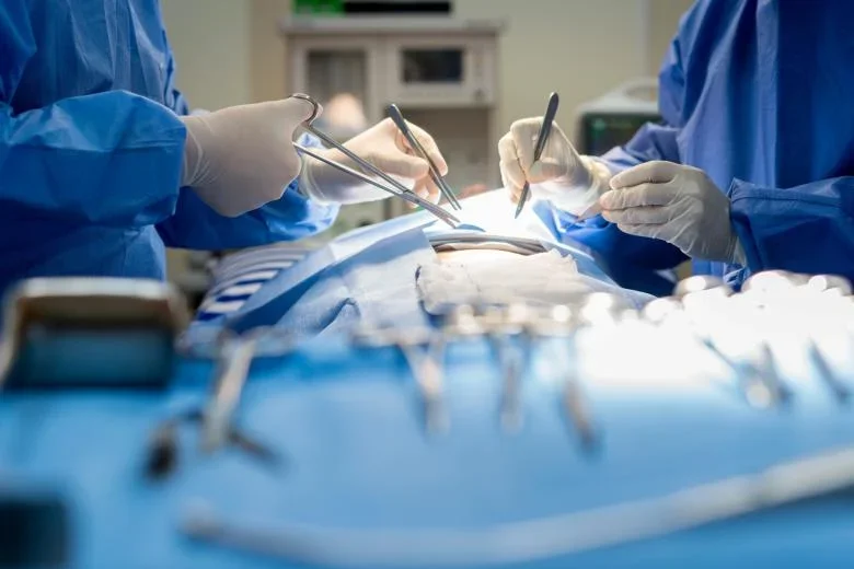Lekarze w niebieskich fartuchach chirurgicznych i rękawiczkach przeprowadzają operację w sali operacyjnej, używając chirurgicznych narzędzi.